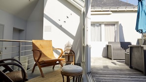 A wooden deck with outdoor furniture, including a chair and a small stool. - Smart Appart (Saint-Nazaire)