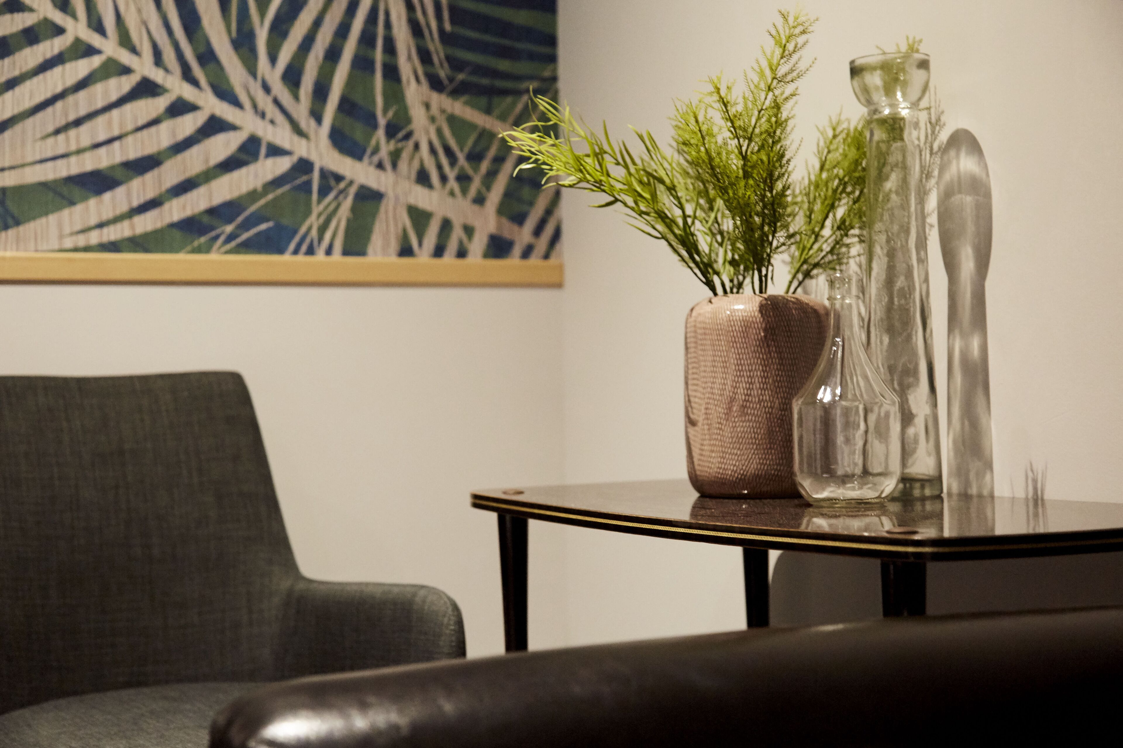 Un salon moderne avec un canapé gris, une petite table sur laquelle est posée une plante en pot et un vase en verre.