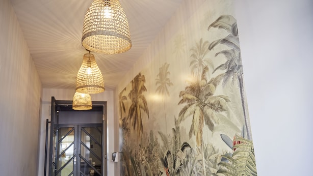 A hallway with woven pendant lights and a mural of tropical plants on the wall. - Smart Appart (Saint-Nazaire)