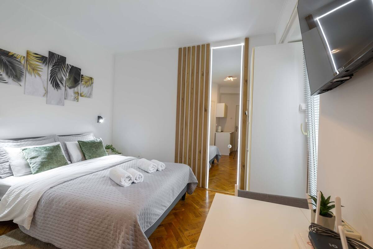 A modern bedroom with a bed, a TV, and a wooden floor.