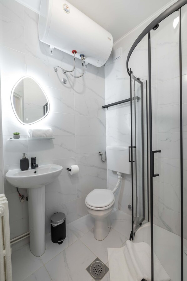 Un baño moderno con lavamanos pedestal, inodoro y ducha con mampara de vidrio.