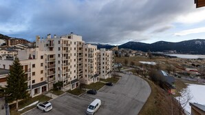 Un edificio residenziale a più piani con balconi, un'area di parcheggio e vista sulle montagne e su un lago.