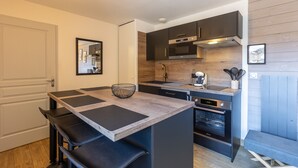 Una cucina compatta con isola centrale, forno integrato e mobili scuri.