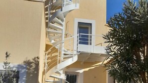 A spiral staircase leading to an upper floor of a building with a beige exterior and a small window. - Superbe T2 Neuf à Carry le Rouet Avec Toit Terrasse Privatif (Carry-le-Rouet)