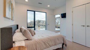 Une chambre moderne avec un grand lit, un téléviseur fixé au mur et une vue sur un pont, visible par la fenêtre.