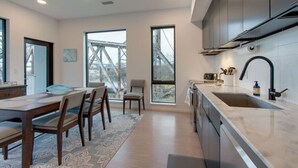 Une cuisine moderne dotée d’une grande fenêtre, un coin repas avec une table et des chaises, et une vue sur un pont à l’extérieur.