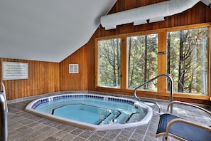A wooden-paneled room with a large window overlooking a forest, a pool with a safety sign, and a video monitoring system notice.