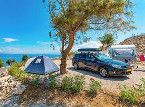 A camping setup with a tent, a car, and a camper parked near a rocky area with a view of the sea.