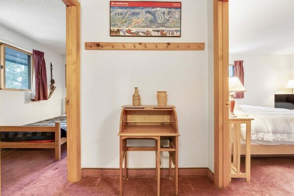 A room with a wooden desk, a bed, a window with curtains, and a wall-mounted picture.