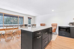 A modern kitchen with a large island, wooden chairs, and a view of the outdoors. - South Ridge G-01 - Sunday River Condo (Newry)