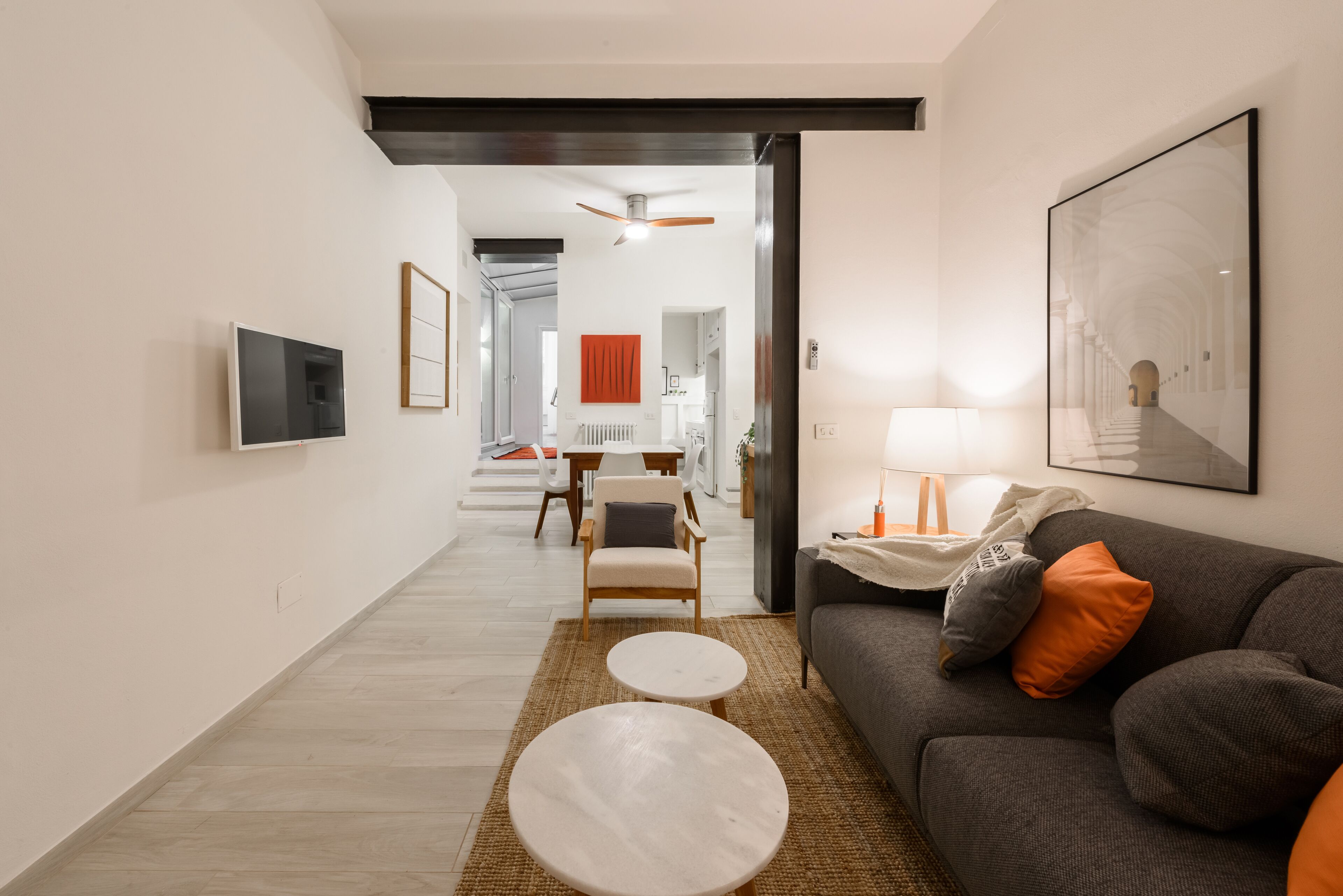 A modern living room with a sofa, two round tables, a TV, and a ceiling fan.