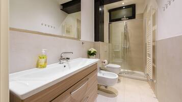 Un baño moderno con un lavamanos grande, tocador, bidé y cabina de ducha con paredes de vidrio.