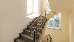 Uma escadaria com corrimãos de metal e degraus de granito, que leva a um patamar com janela com vista para vegetação.