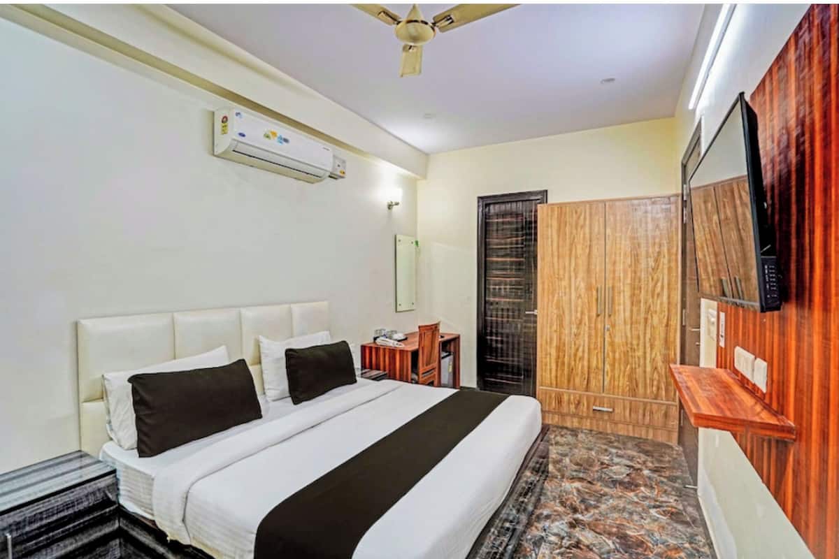 A hotel room with a bed, a desk, a wardrobe, and an air conditioning unit.