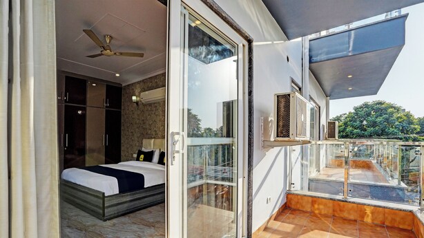 Quarto moderno com uma cama grande, ventilador de teto e varanda com guarda-corpo de vidro.