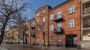 A row of red brick apartment buildings with multiple windows and balconies, a gated entrance, and a clear sky.