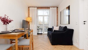 A modern living room with a black sofa, a dining table set with plates and glasses, and a large window with curtains.