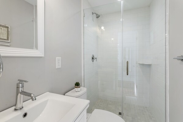A modern bathroom with a white sink, a toilet, and a glass-enclosed shower.