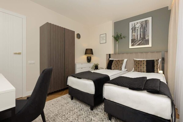 A bedroom with two beds, a desk, a chair, a lamp, and a framed picture on the wall.