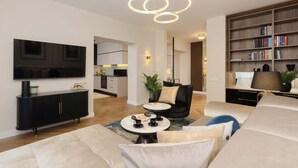 A modern living room with a sofa, a coffee table, a bookshelf, and a flat-screen TV.