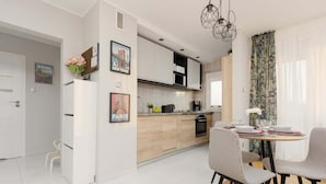 A modern kitchen with white cabinets, a dining area with checkered chairs, and a view of the city through large windows. - Modern Apartment in Zoliborz | Balcony and Workspace (Warszawa)