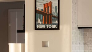 A dining area with a table set for two, a framed Brooklyn Bridge poster, a framed Eiffel Tower poster, and a light switch on the wall. - Modern Apartment in Zoliborz | Balcony and Workspace (Warszawa)