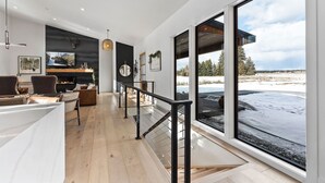 A modern interior with a wooden floor, a fireplace, a seating area with leather chairs, and a large window offering a snowy outdoor view.