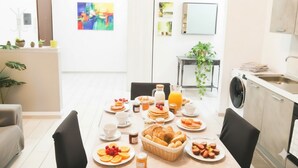 Cocina moderna con zona de comedor, mostrando un desayuno con panqueques, frutas y bebidas.