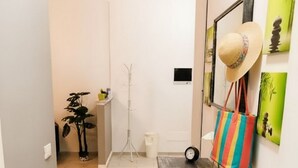 Un pasillo con una mesa de madera, un sombrero y un bolso colorido. Se observa un perchero y una planta al fondo.