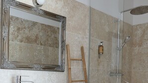 Un baño con lavamanos de mármol, tocador de madera, espejo, ducha con puerta de vidrio y una escalera apoyada en la pared.