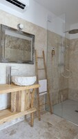Un baño con lavamanos de mármol, tocador de madera, espejo, ducha con puerta de vidrio y una escalera apoyada en la pared.