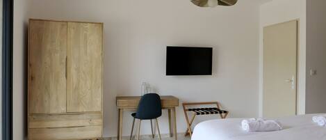 Habitación de hotel con armario de madera, escritorio con silla, televisor montado en la pared y cama con toallas.