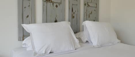 A bed with white bedding and pillows, set against a wall with distressed white panels.