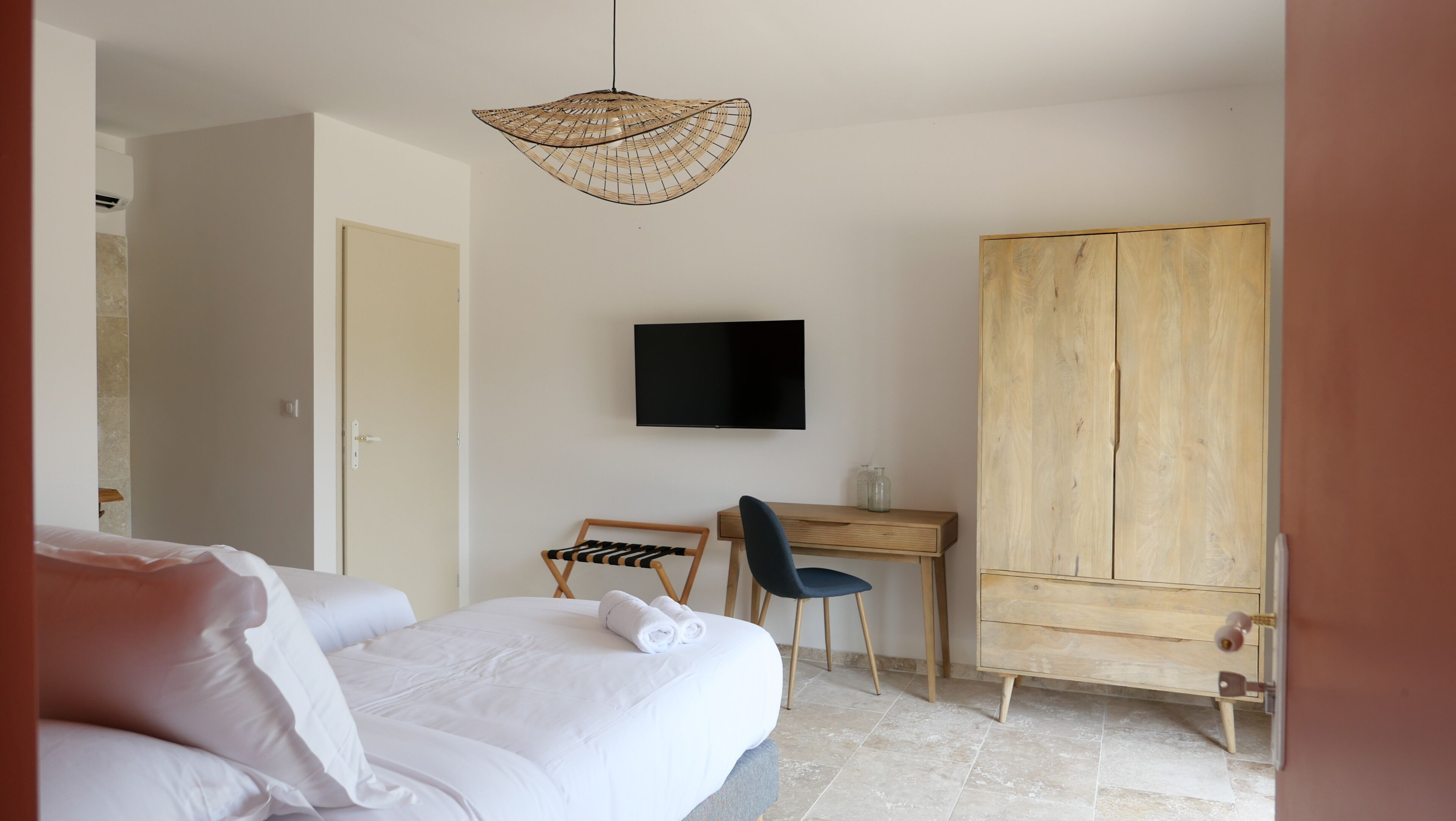 Habitación de hotel con cama, escritorio, silla, armario y televisor en la pared.