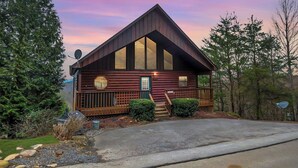 Une cabane en rondins avec un toit à pignon très incliné, une véranda à l’avant et une antenne parabolique.
