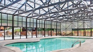 Une grande piscine intérieure dotée d’un toit en verre, entourée de chaises longues et offrant une vue sur l’extérieur.