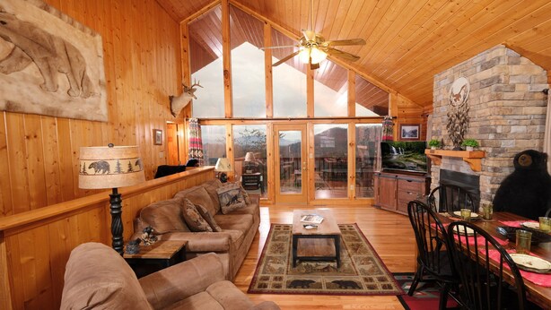 L’intérieur chaleureux d’un chalet, avec un revêtement mural en bois, une cheminée en pierre et un coin repas comprenant une table et des chaises.
