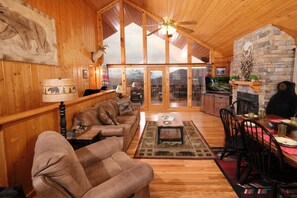 A cozy cabin interior with a wooden interior, a stone fireplace, and a dining area with a table and chairs. - Dream Catcher: Catch Your Perfect Escape (Sevierville)