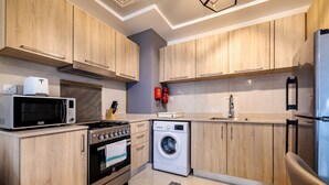 A modern kitchen with wooden cabinets, a microwave, stove, washing machine, and a refrigerator. - Tanin - Sleek Studio in AG Tower with Canal Views (Dubai)