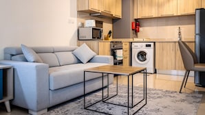 A modern living room with a grey sofa, a wooden coffee table, and a washing machine in the background. - Tanin - Sleek Studio in AG Tower with Canal Views (Dubai)