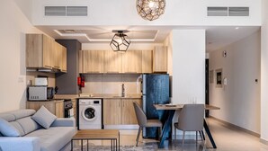 A modern kitchen with wooden cabinets, a built-in washing machine, and a dining area with a table and chairs. - Tanin - Sleek Studio in AG Tower with Canal Views (Dubai)