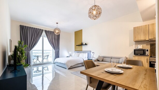 A modern hotel room with a large bed, a dining table, a kitchen area, and a balcony with a view. - Tanin - Sleek Studio in AG Tower with Canal Views (Dubai)