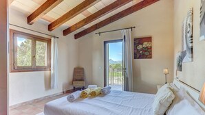 A bedroom with a bed, a chair, a balcony door, and a painting. - S'Albufereta by Rentallorca (Alcúdia)