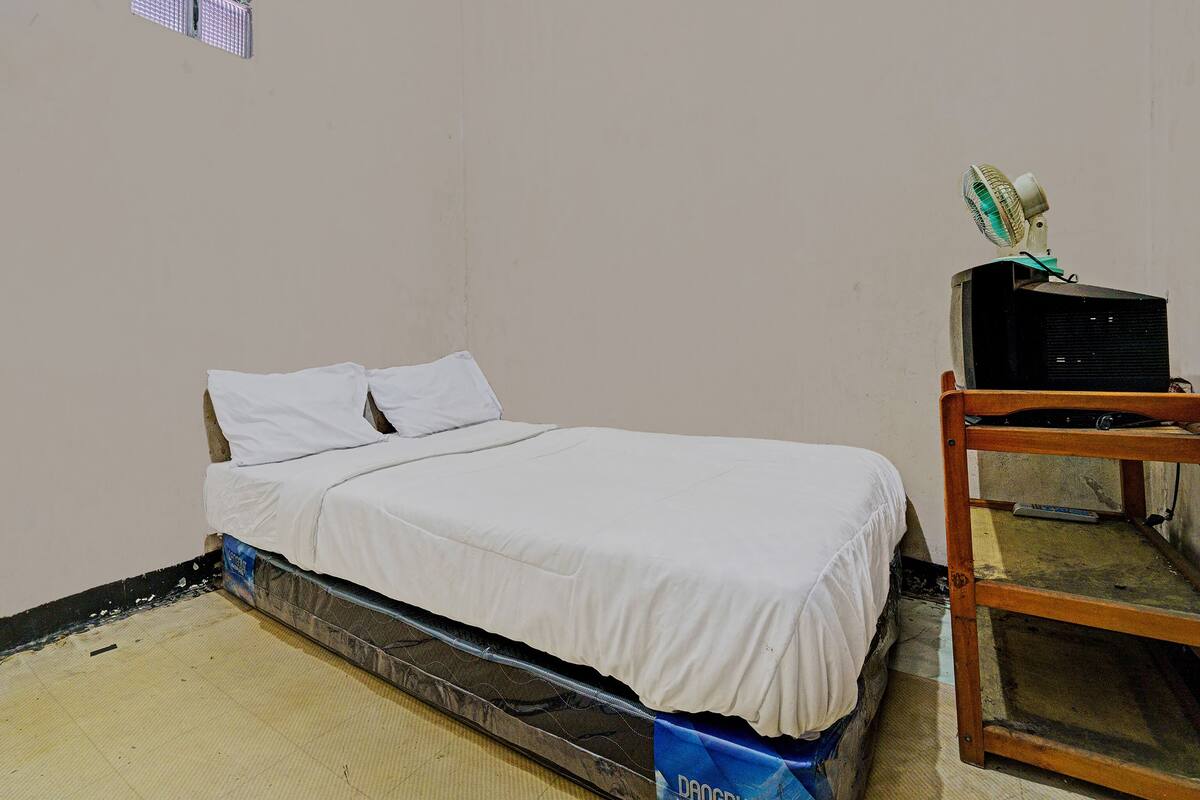 A small, sparsely furnished room with a single bed, a wooden nightstand, and a television on a stand.