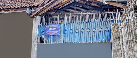 Propiedad resguardada por un portón con un letrero azul que indica 'BRADJA KOST NO.04' y un número de contacto.