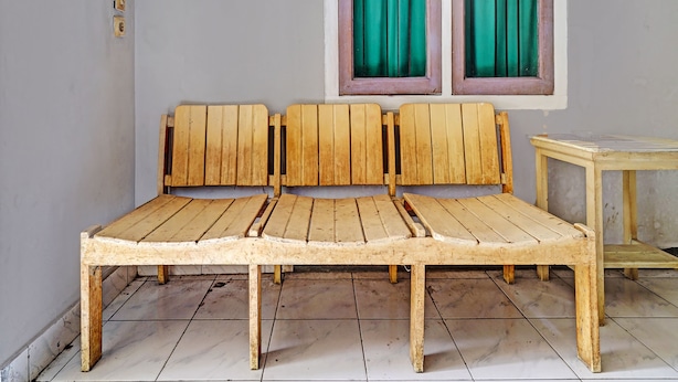 A simple wooden bench with a backrest and a small table beside it, in a room with a tiled floor and a window with green curtains. - OYO Life 92709 Kost Teras Cikapundung Syariah (Bandung)