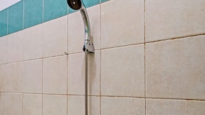 A shower with a handheld showerhead mounted on a wall with beige tiles and a teal border. - OYO Life 92709 Kost Teras Cikapundung Syariah (Bandung)