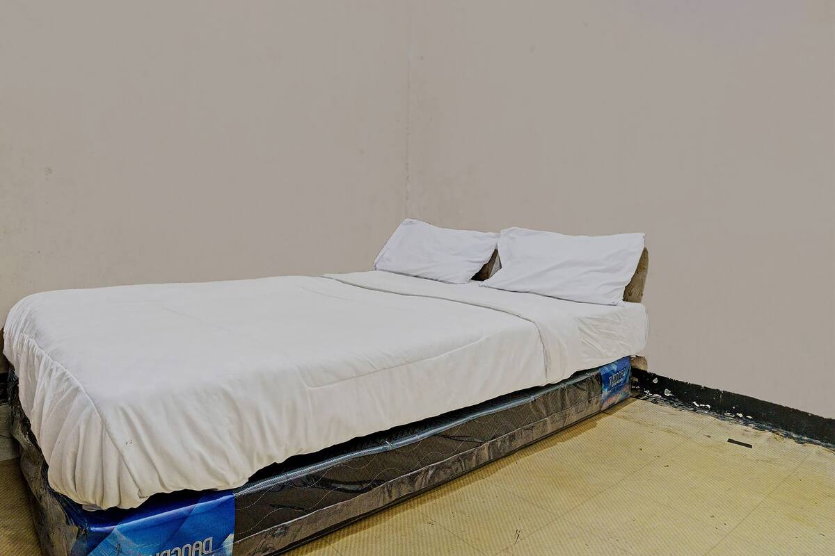A single bed with white bedding in a room with plain walls and a visible mattress protector.