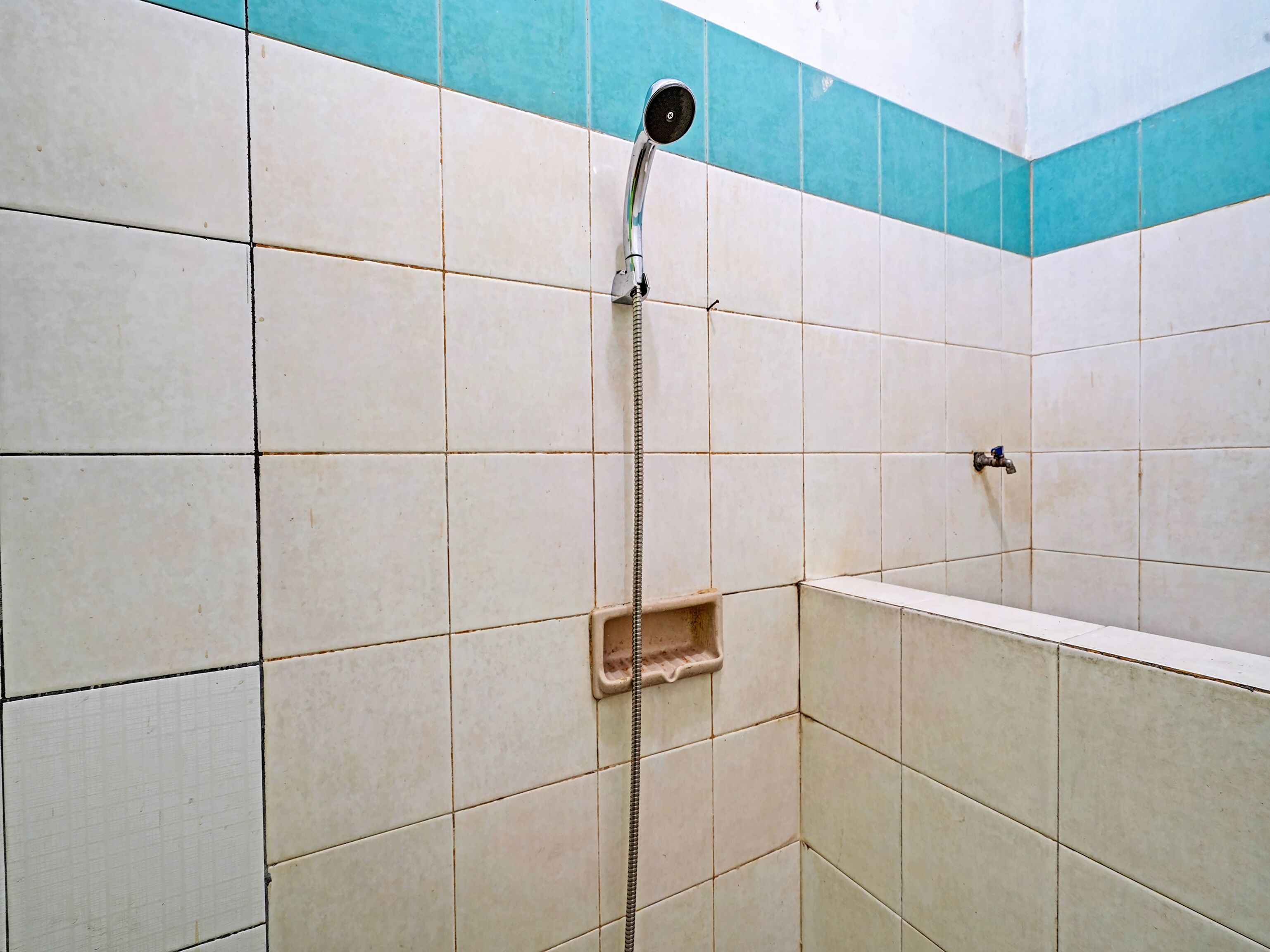 A shower area with white and blue tiles, a showerhead, and a small shelf.