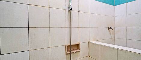 A shower area with white and blue tiles, a showerhead, and a small shelf.